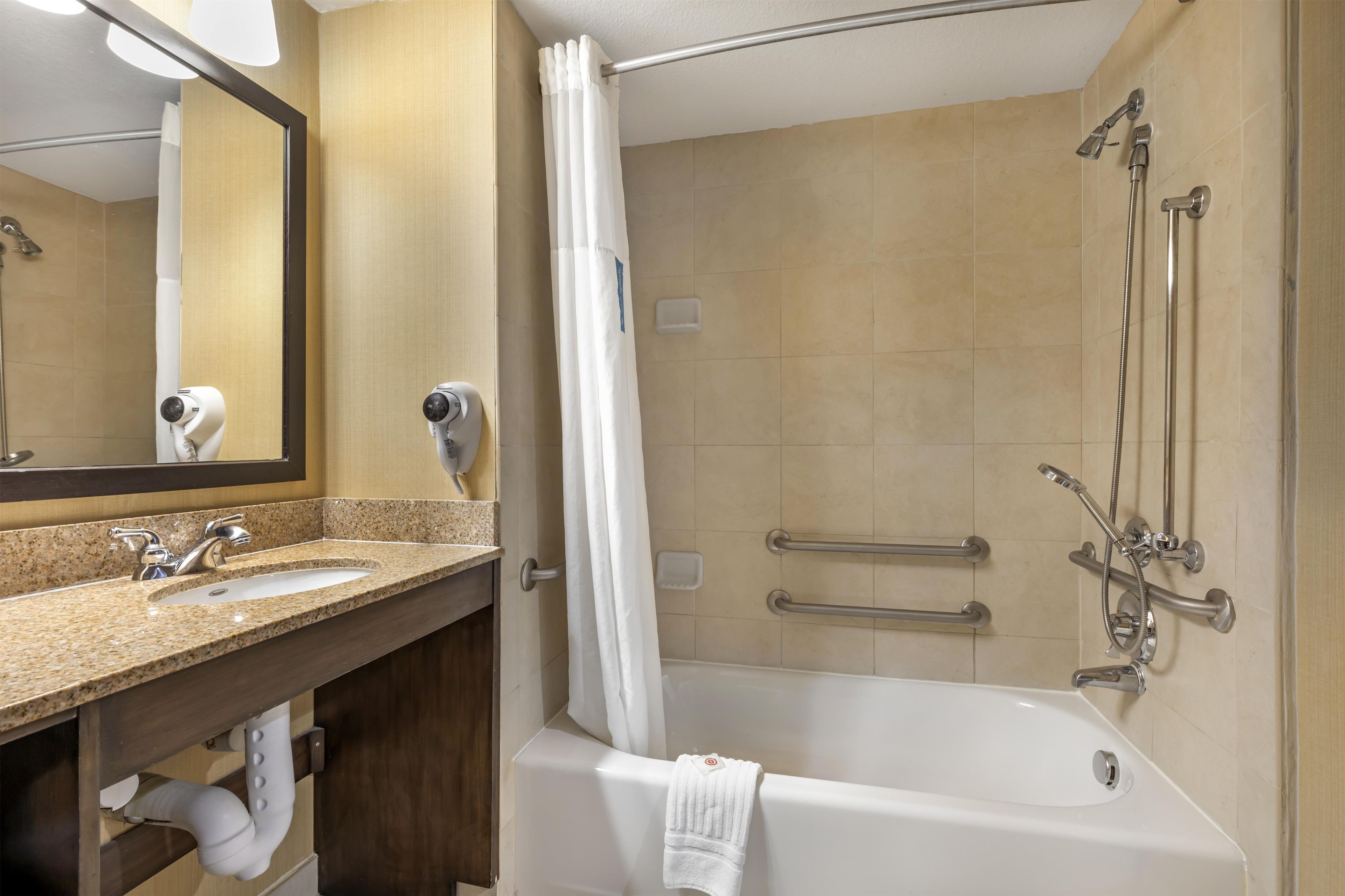 Une salle de bain équipée d’un lavabo, d’un miroir, d’un porte-serviettes, d’une douche et de barres d’appui.