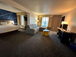 A hotel room with a bed, sofa, armchair, small round table, and a TV on a stand. - Best Western Plus Frisco East - McKinney (Frisco)