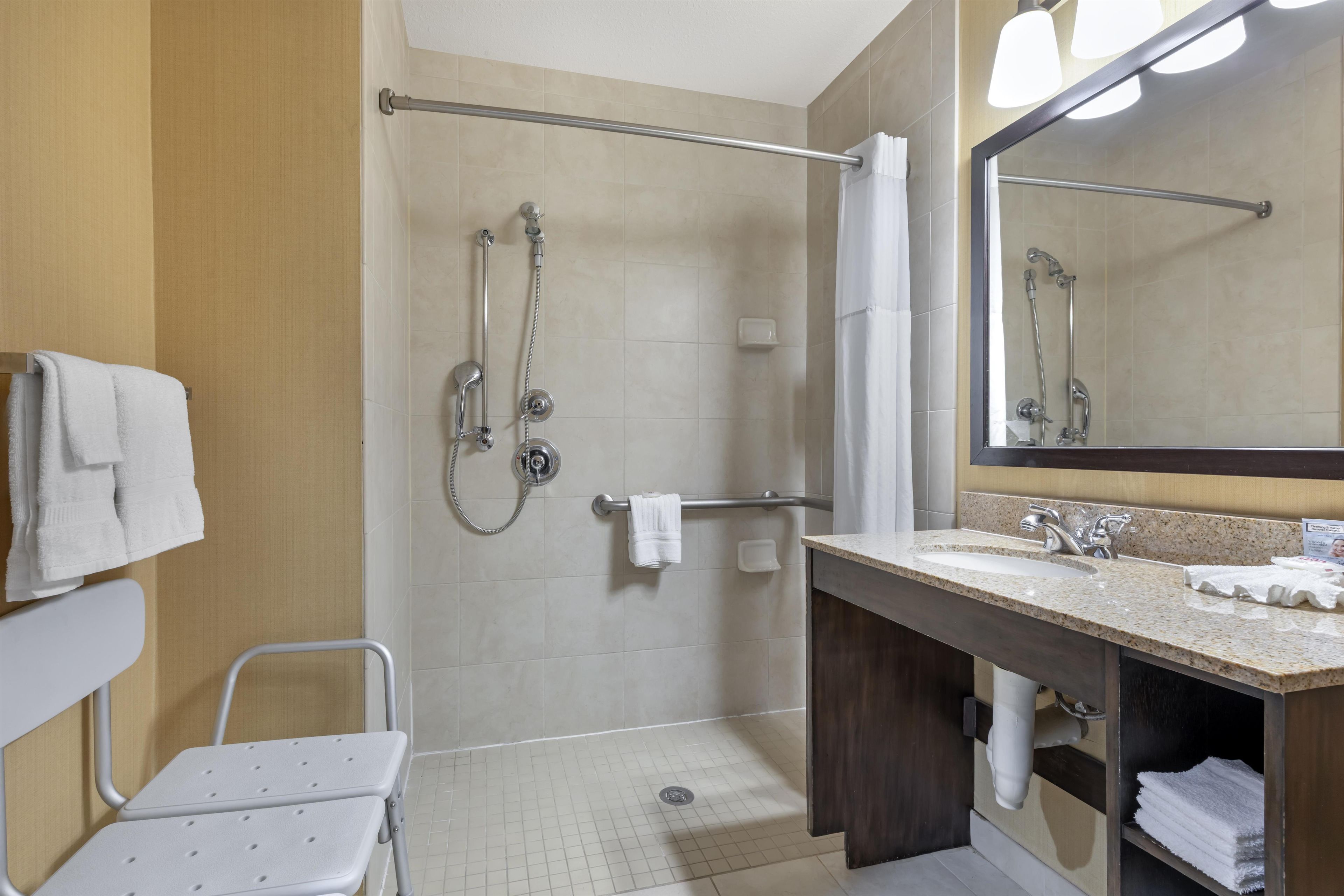 Un baño de hotel con ducha, lavamanos, espejo y una silla.