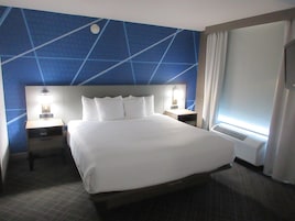 Habitación de hotel con una cama grande, dos mesitas de noche con lámparas, un cabecero con diseño geométrico y una ventana con cortinas.