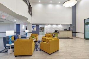 Um hall espaçoso com balcão de recepção, área de estar e uma grande obra de arte na parede.