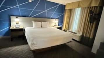 Habitación de hotel con una cama grande, una mesita de noche con lámpara y una ventana con cortinas.