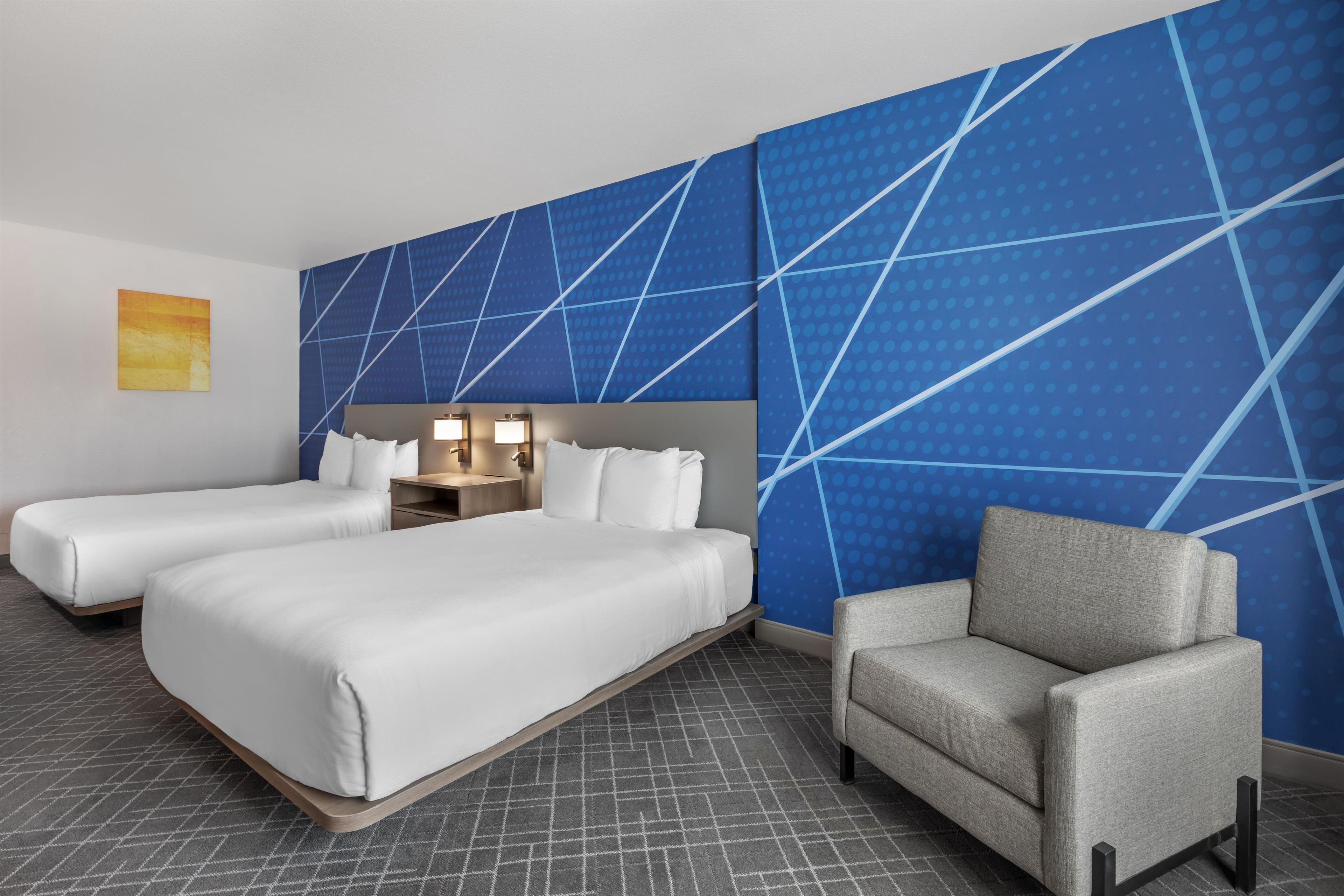 Habitación de hotel con dos camas, zona de estar y una pared con diseño geométrico.