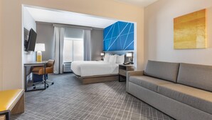 A hotel room with a bed, a desk, a chair, a sofa, and a large abstract painting on the wall. - Comfort Inn & Suites Frisco East - McKinney (Frisco)