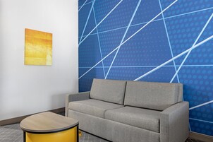Quarto moderno com sofá cinza, mesa lateral amarela e parede azul com padrão geométrico.