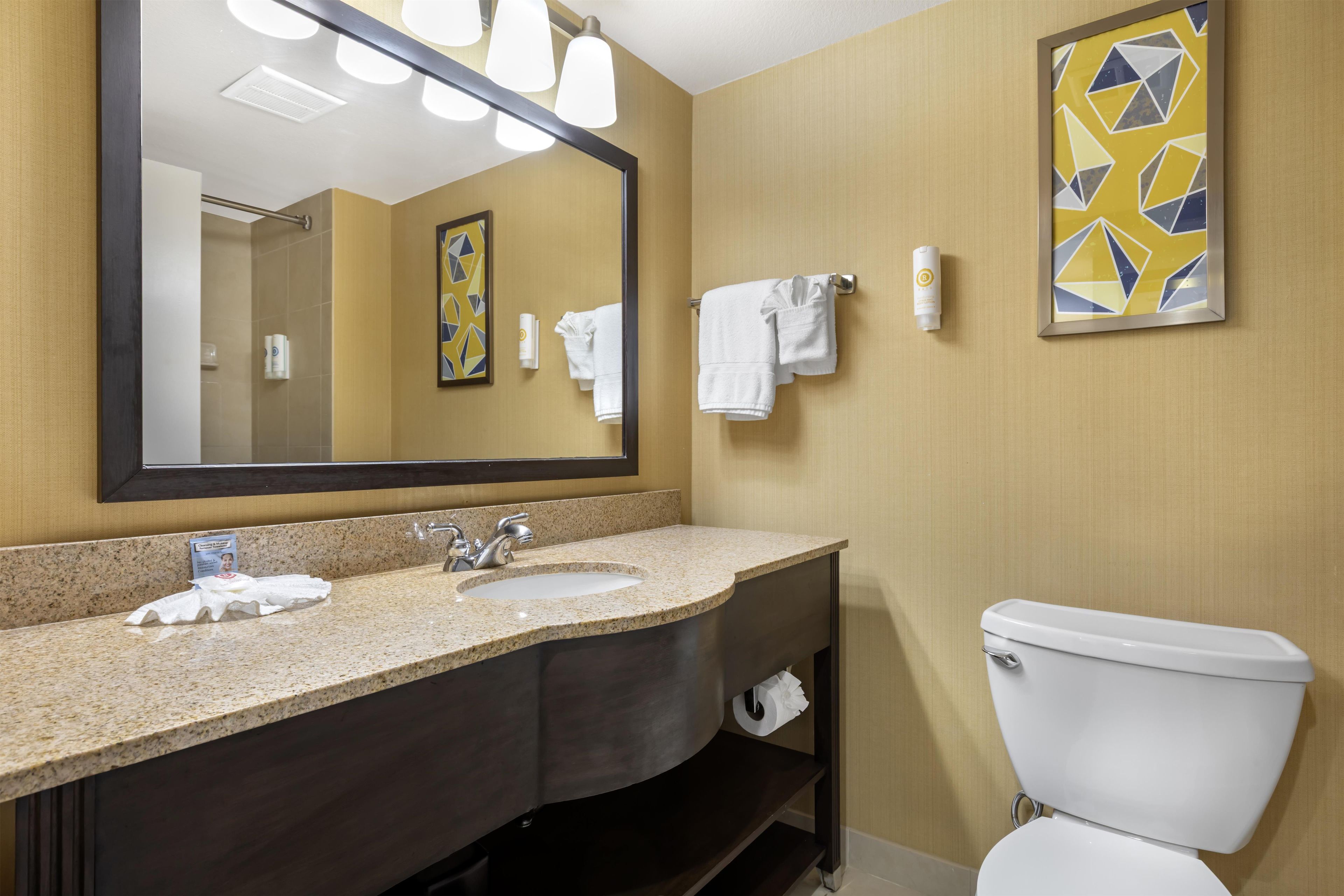 A bathroom with a sink, mirror, towel rack, toilet, and a framed abstract painting on the wall.