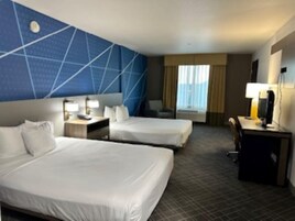 A hotel room with two beds, a desk, a chair, and a TV.
