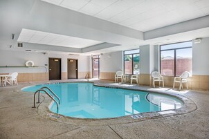 Una piscina con agua cristalina, rodeada de sillas y mesas blancas, y un suelo de baldosas.