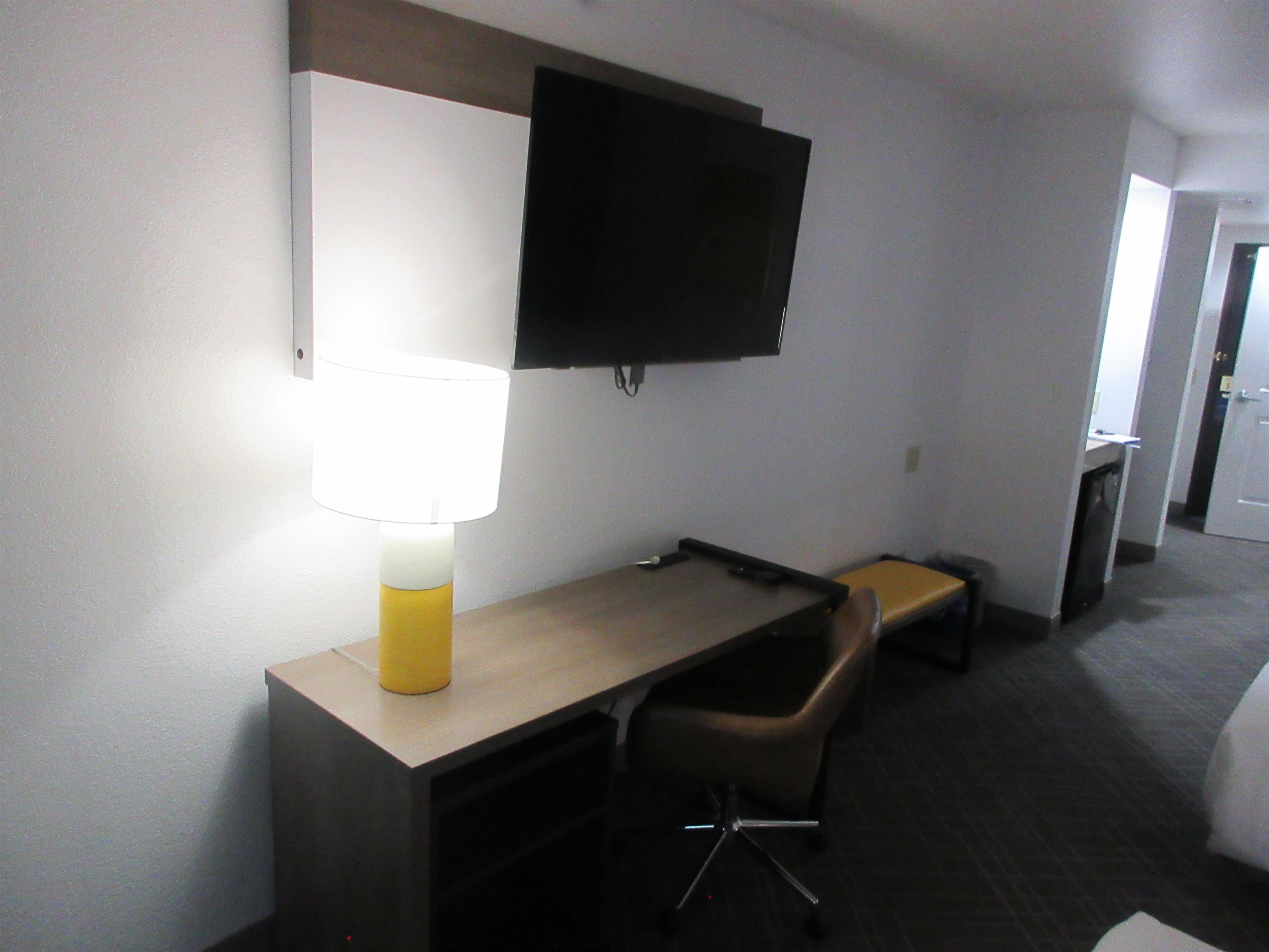 Una habitación de hotel con escritorio, silla, lámpara, televisión y una mesita.