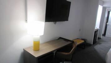 Una habitación de hotel con escritorio, silla, lámpara, televisión y una mesita.