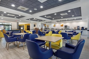 Una cafetería con mesas y sillas, una barra con equipo de servicio de alimentos y un techo con iluminación empotrada.