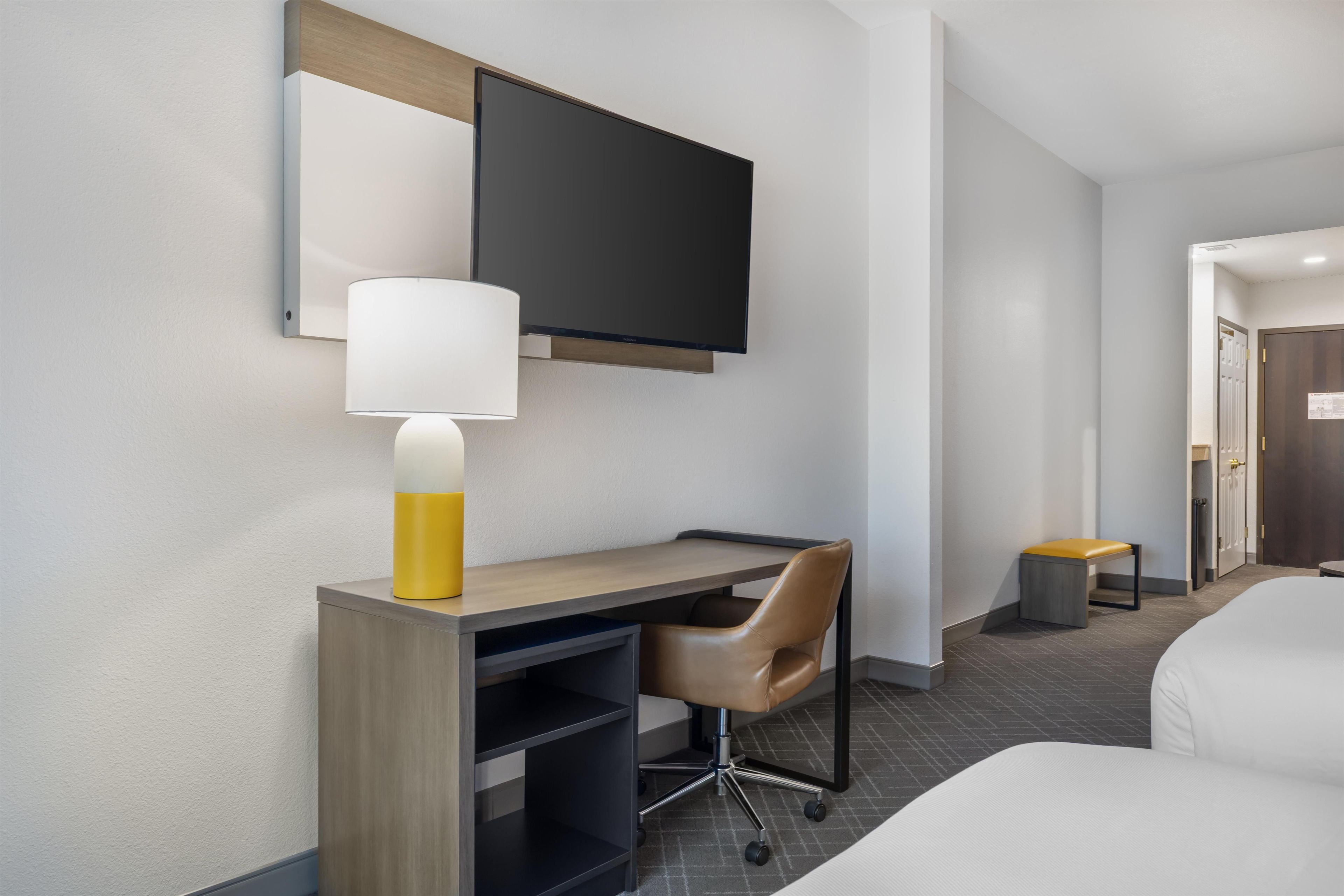 A hotel room with a bed, a desk with a chair, a television, and a lamp.