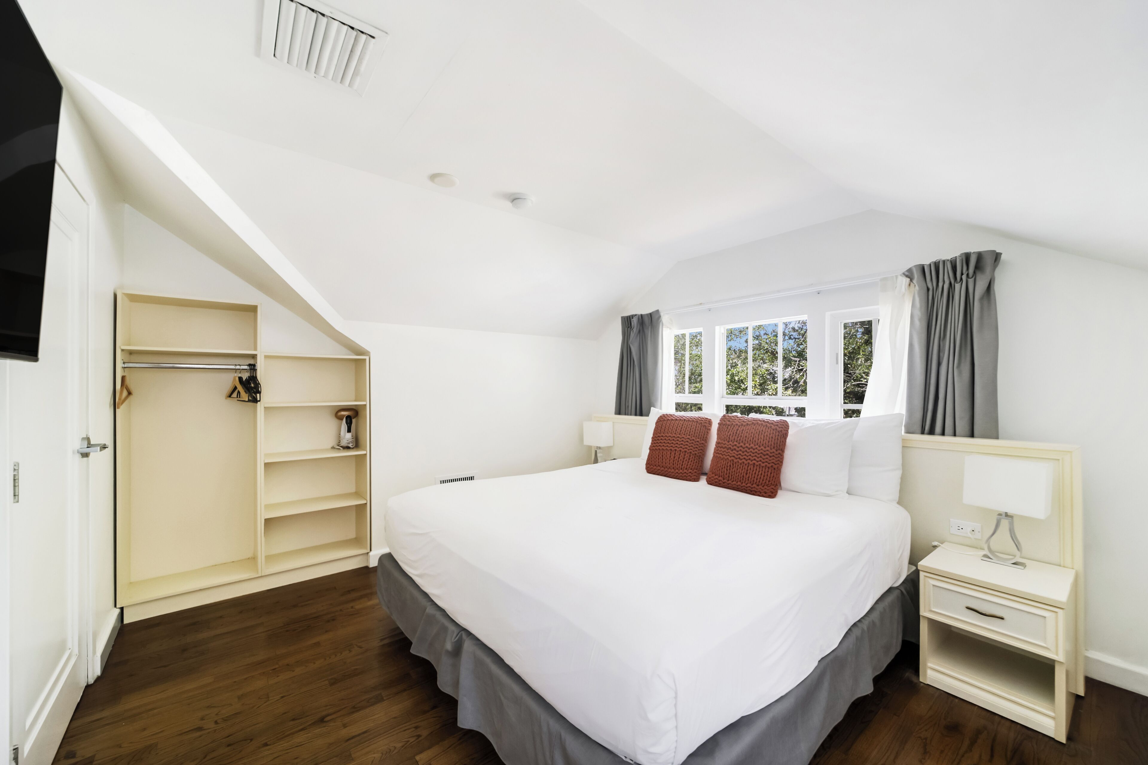 Un dormitorio con una cama grande, una mesita de noche, un armario y una ventana con cortinas.