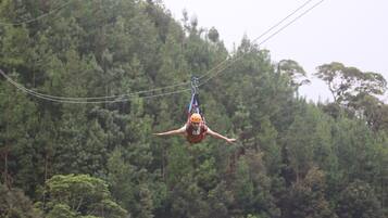 A person suspended in mid-air, wearing a helmet and harness, with a forested background.