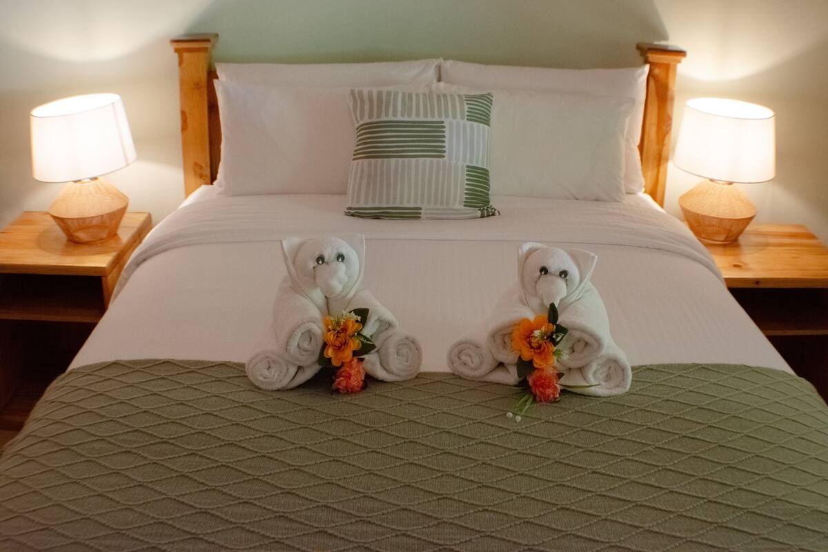 Una cama bien hecha con dos osos de peluche, un edredón verde y dos lámparas de noche.