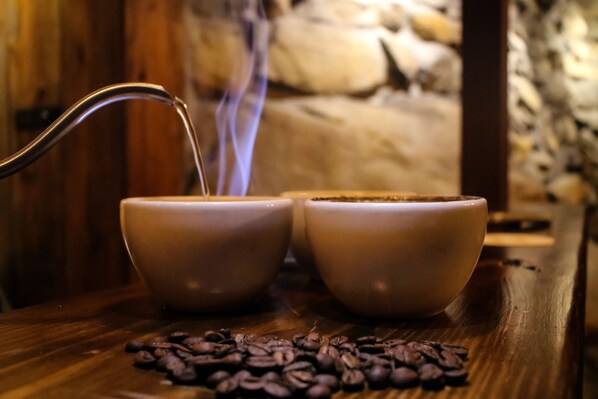 Dos tazas blancas de cerámica sobre una mesa de madera con granos de café esparcidos.