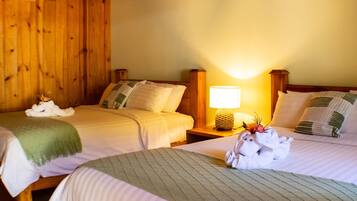 Habitación de hotel con dos camas, cabeceros de madera, una mesita de noche con lámpara y toallas sobre las camas.