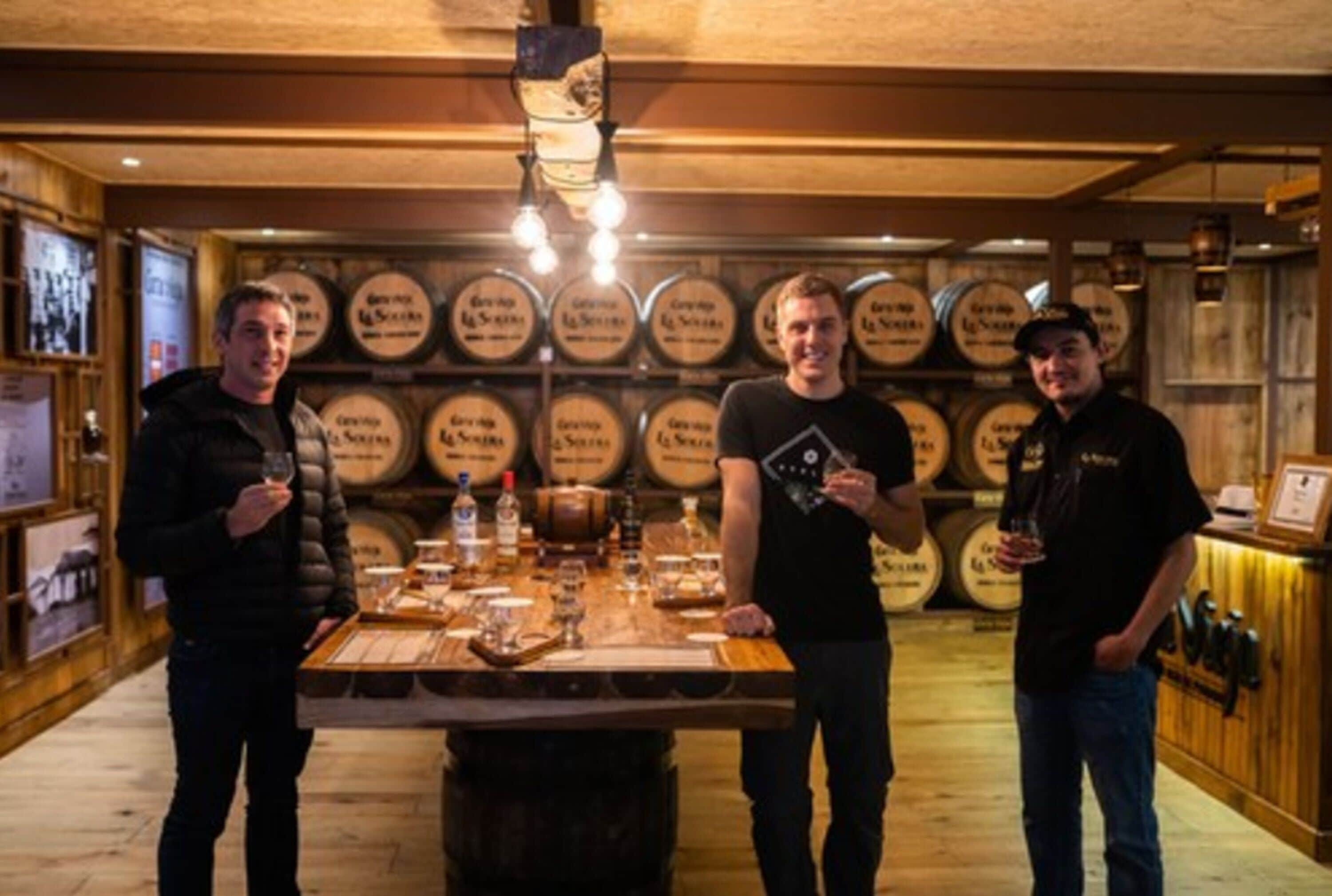 Uma área de bar com barris de madeira, balcão de madeira e uma pessoa segurando um copo.