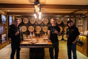 Una zona de bar con barriles de madera, una barra de madera y una persona sosteniendo un vaso.