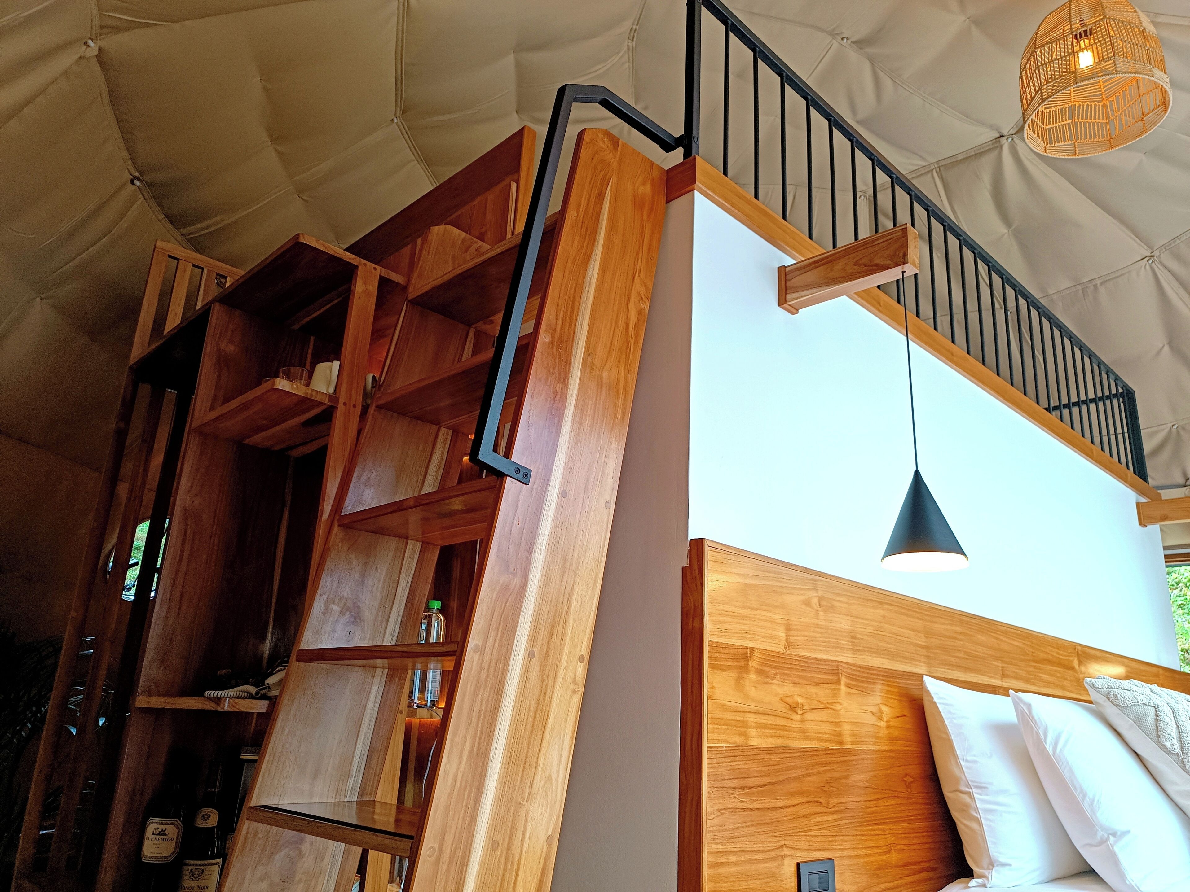 A wooden staircase with a black railing leading to a loft area.