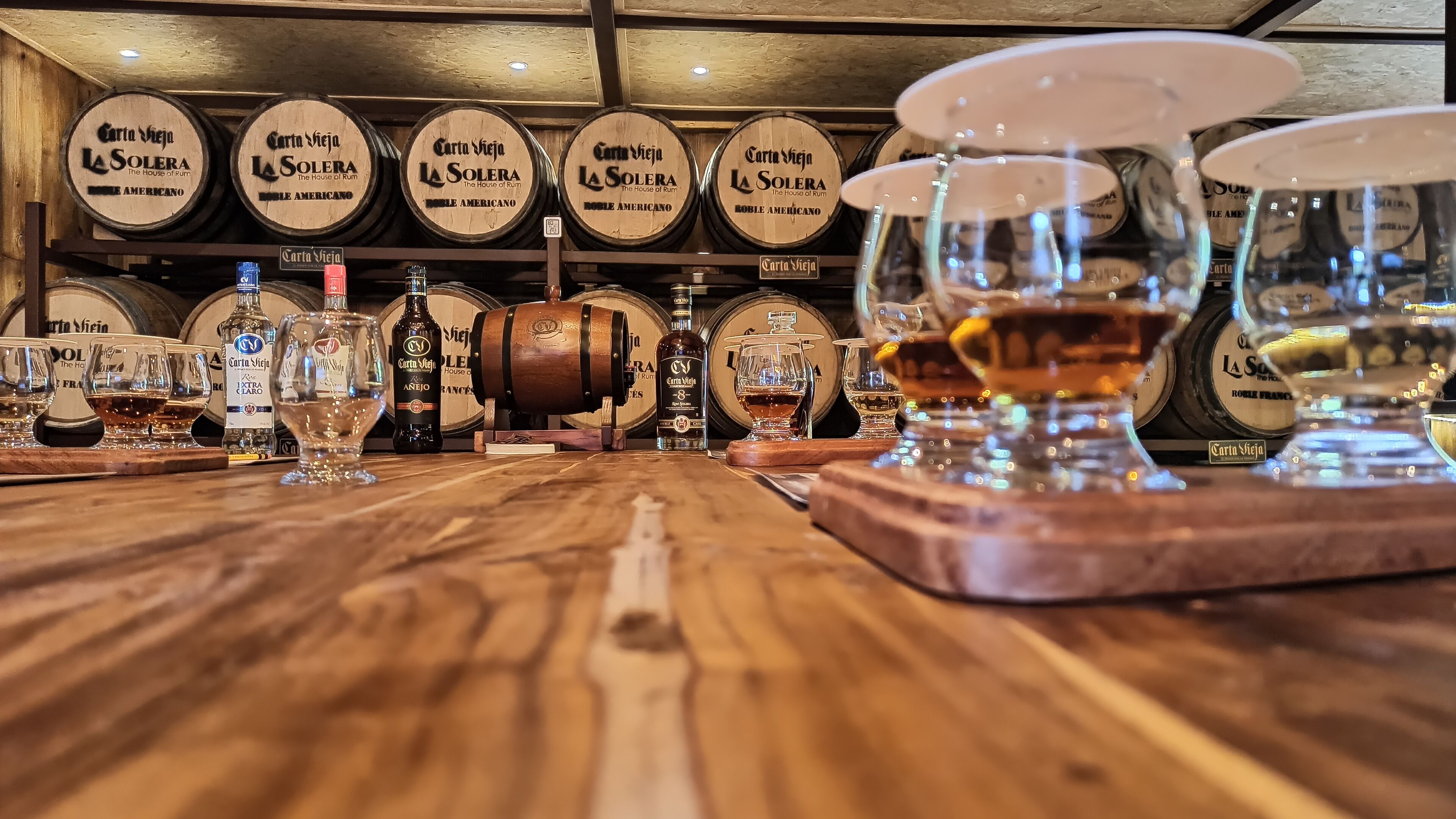 A bar area with wooden barrels labeled 'Carta Vieja La Solera' and 'The House of Rum' behind the bar.