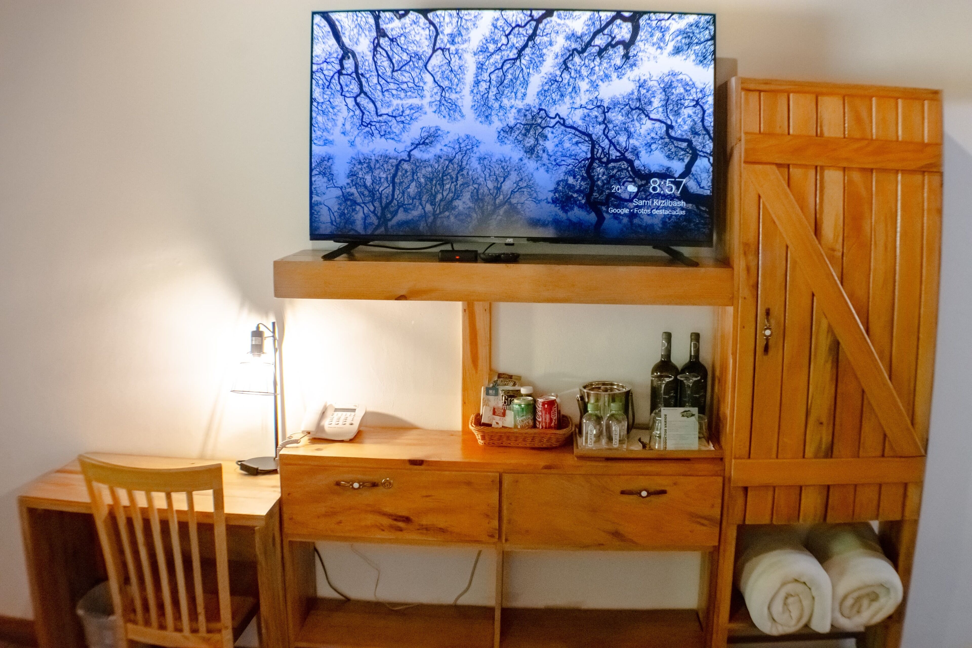 A wooden desk with a television displaying a forest scene, a phone, and a basket with bottles and cans.