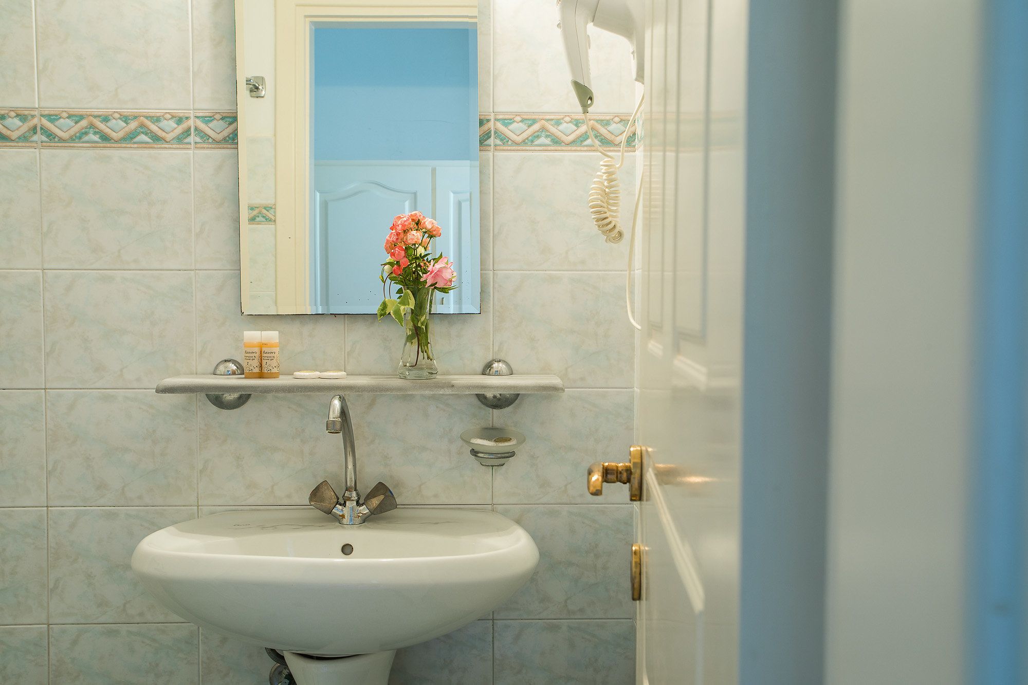 A bathroom with a white sink, a mirror, and a vase with flowers.