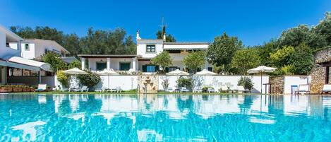 Una piscina al aire libre, sombrillas, sillones reclinables de piscina