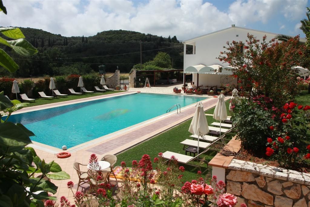 Piscina rectangular con sillas de descanso y sombrillas, rodeada por un muro de piedra y abundante vegetación.