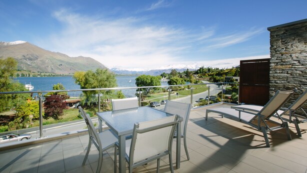 A balcony with a glass table and chairs, overlooking a lake and mountains. - Lakeside Apartments (Wanaka)