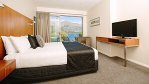 A hotel room with a large bed, a TV, a desk, and a view of a mountain and lake. - Lakeside Apartments (Wanaka)