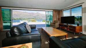 A modern living room with a large window, a leather sofa, a wooden coffee table, and a flat-screen TV. - Lakeside Apartments (Wanaka)