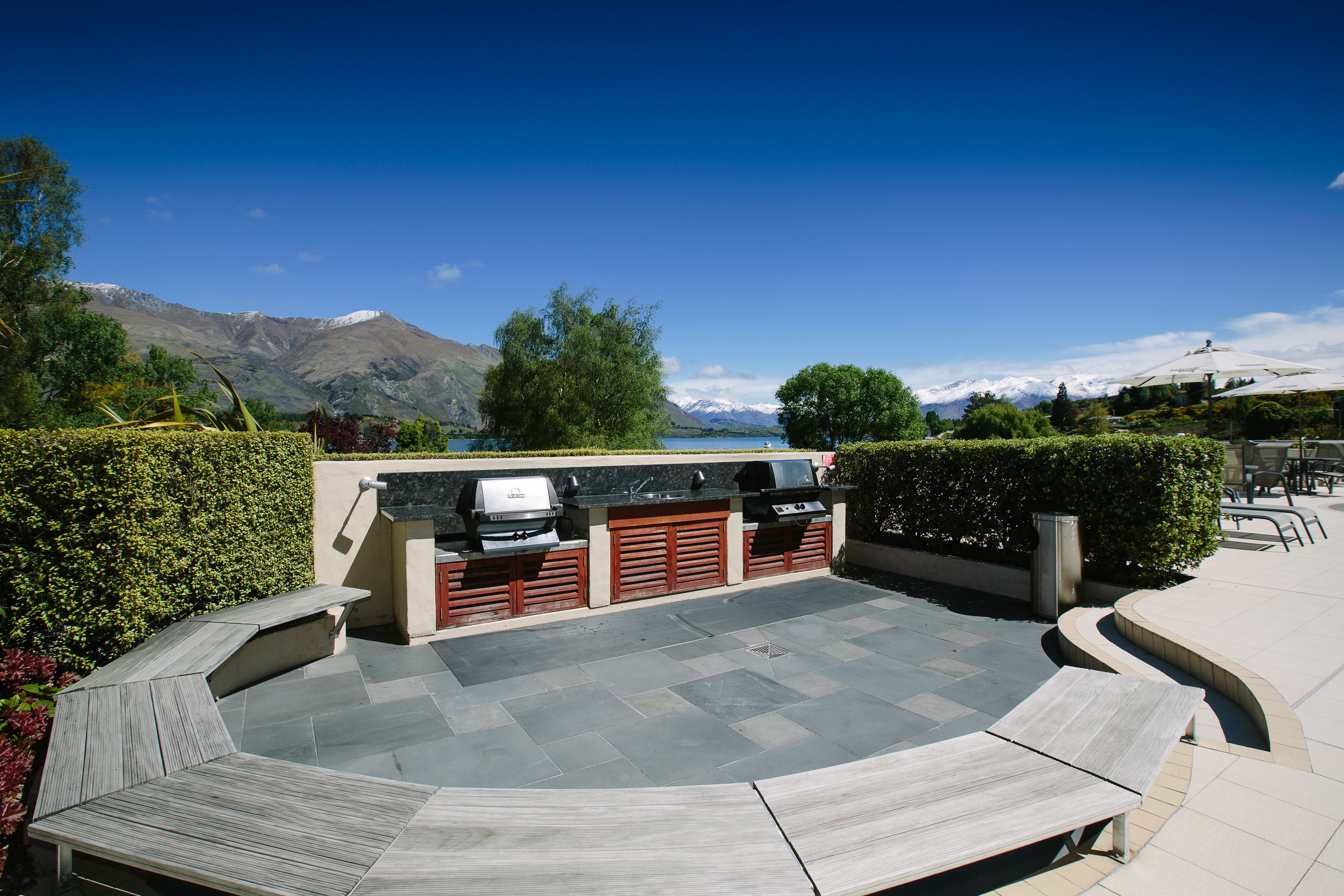 An outdoor patio with a barbecue area, seating, and a view of mountains and a lake.