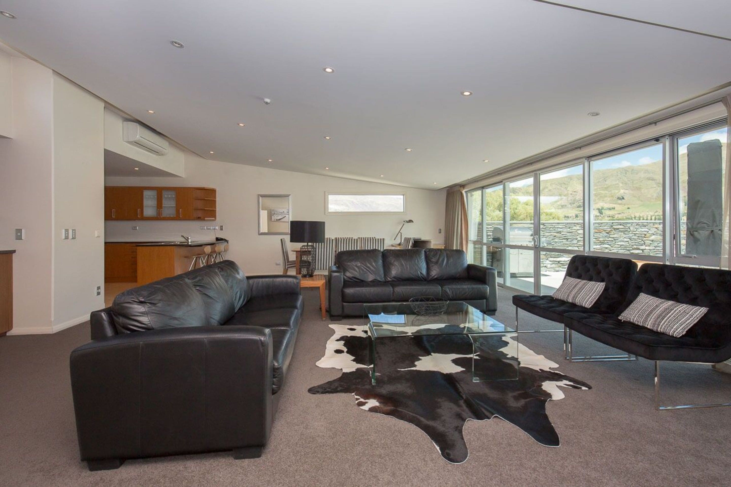 A modern living room with leather sofas, a glass coffee table, and a cowhide rug.