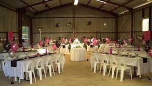 Un salón amplio con mesas dispuestas para un evento, con globos y un escenario.