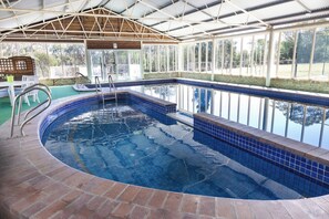 An indoor swimming pool with a tiled edge, a wooden deck area, and a covered roof structure. - Madison's Mountain Retreat (Kurrajong Heights)