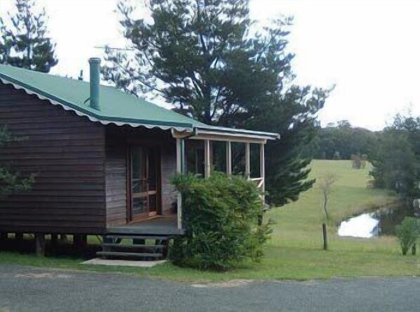 A rustic cabin with a porch, surrounded by greenery and a small pond. - Madison's Mountain Retreat (Kurrajong Heights)
