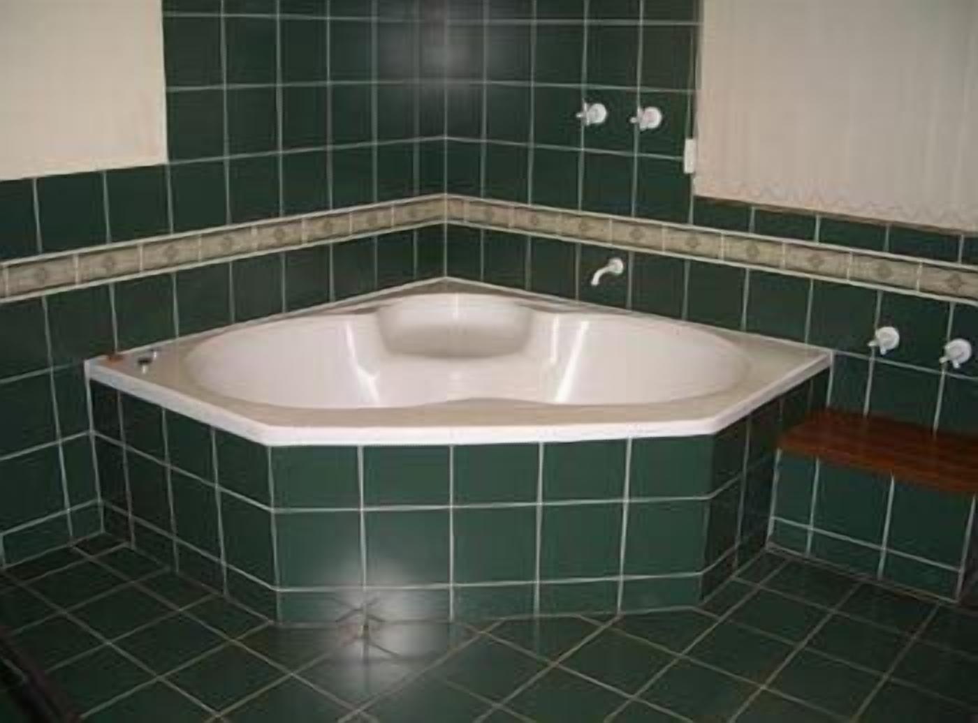 A bathroom with a freestanding bathtub, green tiles, and a wooden bench.