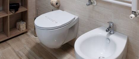A modern bathroom with a toilet, bidet, and a shelf with toiletries.