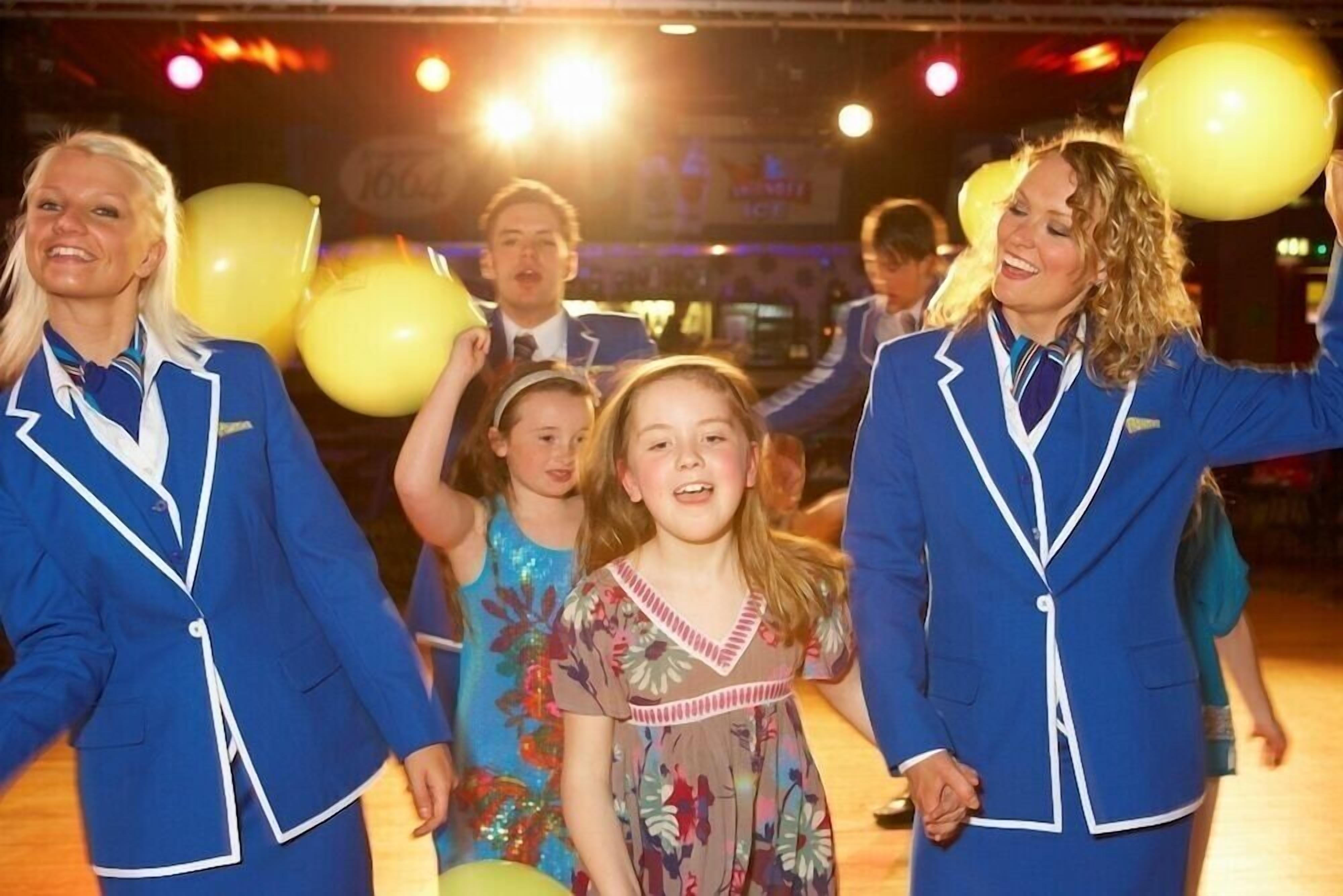 A group of people in blue uniforms holding yellow balloons at an indoor event.