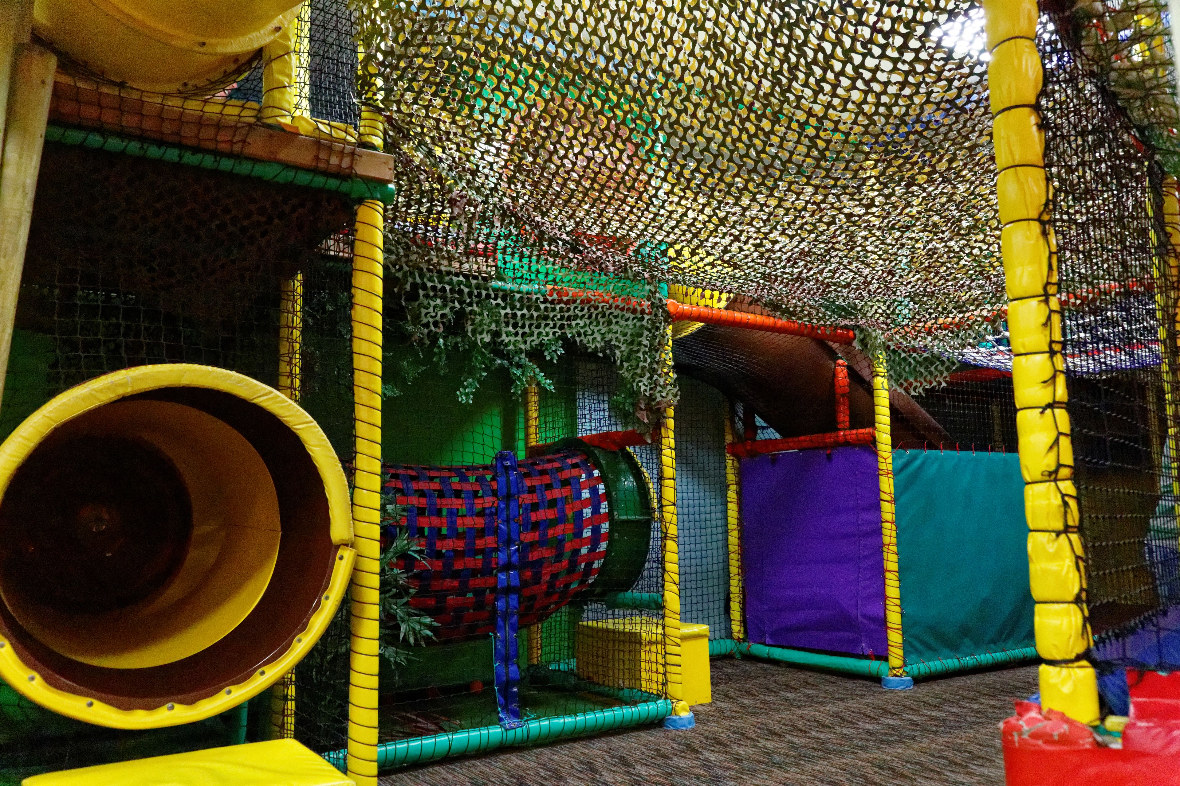 An indoor play area with a netted climbing structure, a tunnel, and various play elements.