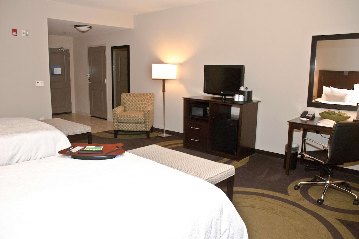 A hotel room with two beds, a desk with a chair, a television, and a desk lamp.
