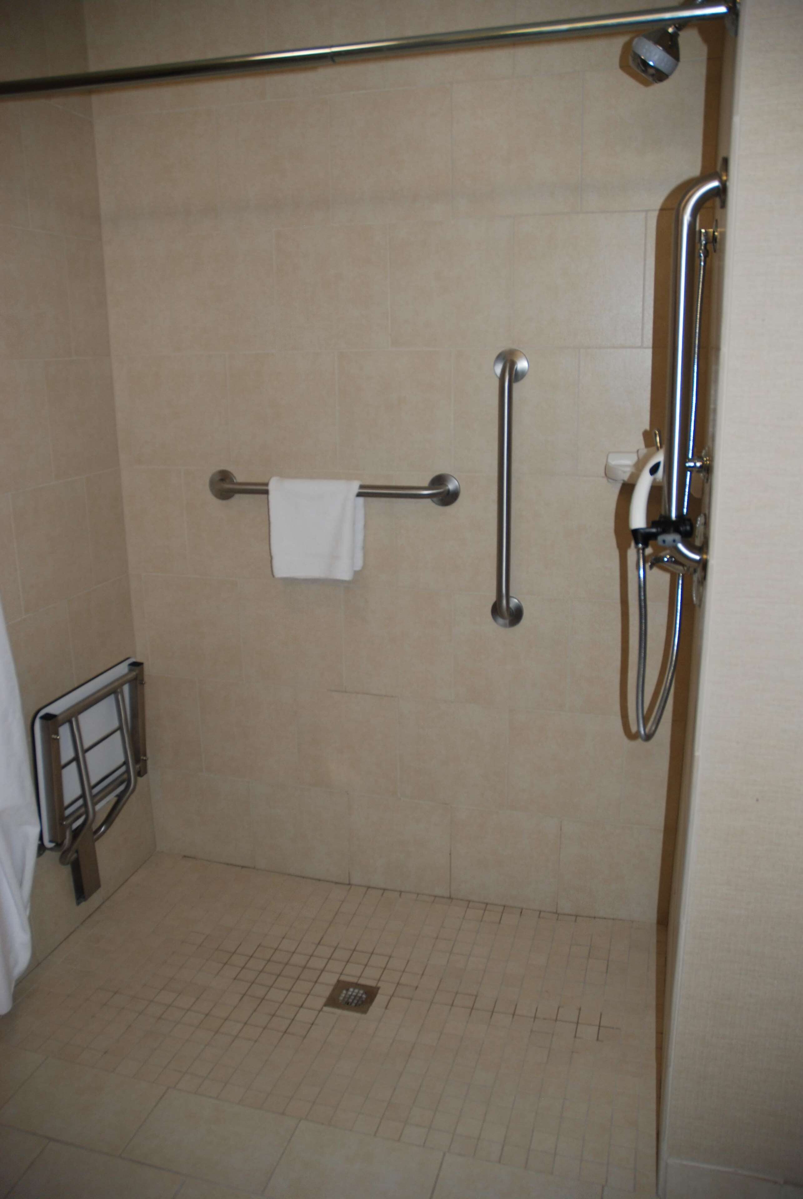 Un área de ducha con barra de apoyo, toallero y cabezal de ducha de mano.