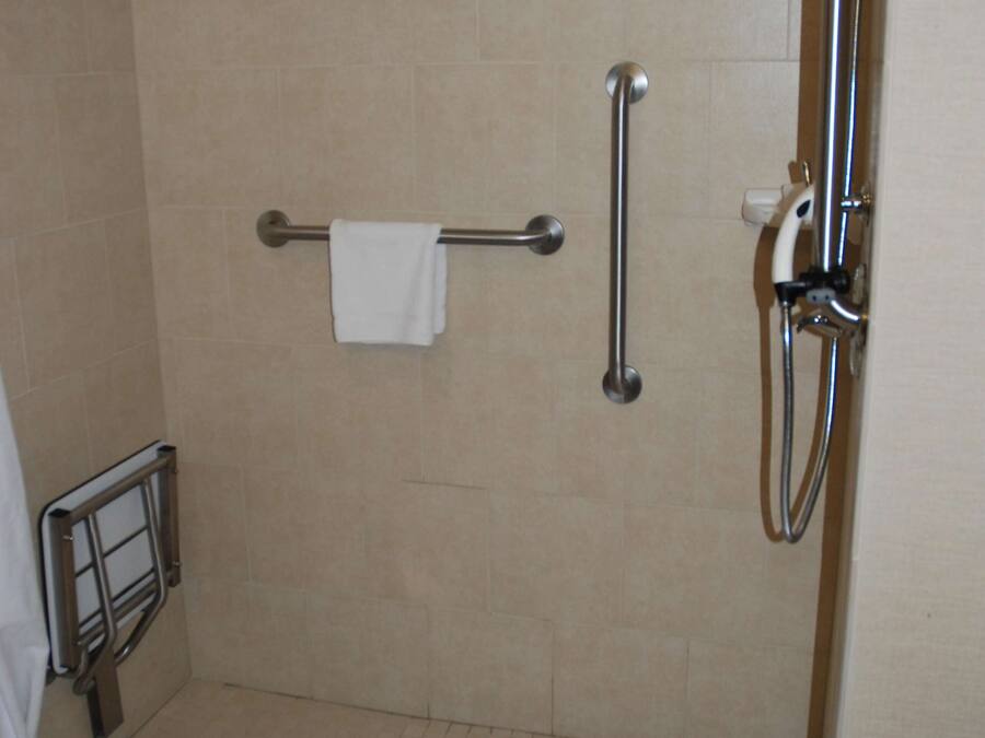 Uma área de chuveiro com barra de apoio, porta-toalhas e chuveiro manual.