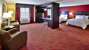 Une chambre d’hôtel avec un tapis rouge, deux lits, un bureau avec une télévision, une chaise et une lampe.