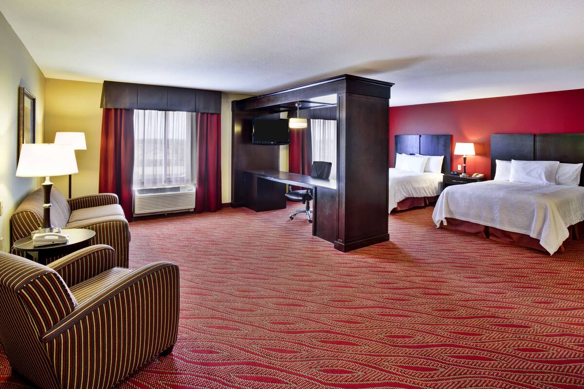 Une chambre d’hôtel avec un tapis rouge, deux lits, un bureau avec une télévision, une chaise et une lampe.
