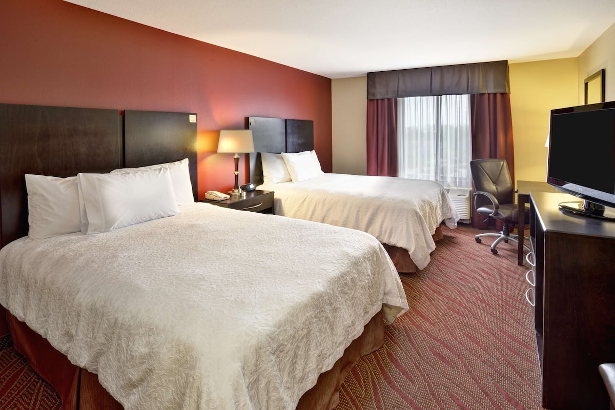 Une chambre d’hôtel avec deux lits, un bureau avec une télévision, une chaise et une fenêtre avec des rideaux.