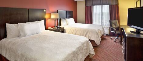 A hotel room with two beds, a desk with a TV, a chair, and a window with curtains.