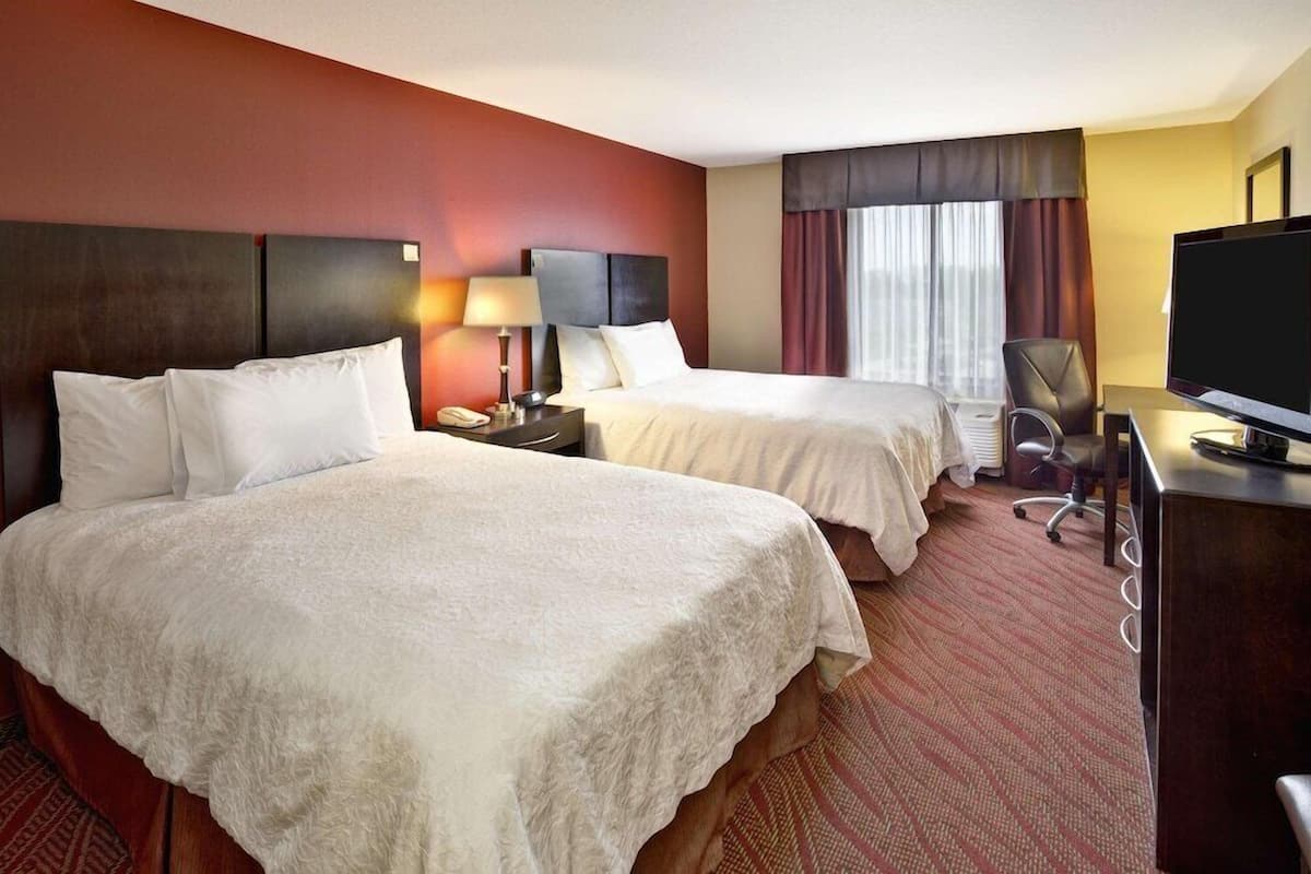 Une chambre d’hôtel avec deux lits, un bureau, une télévision et une fenêtre avec des rideaux.