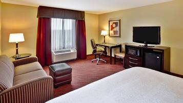 A hotel room with a bed, a desk with a computer, a chair, and a television.